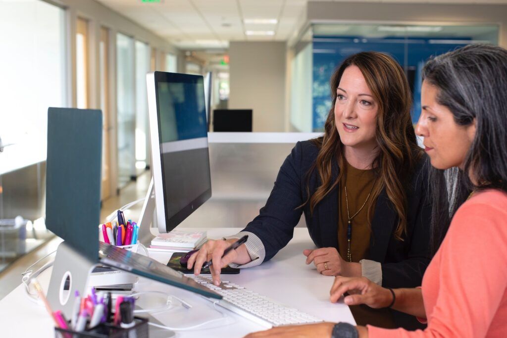 Two women sitting in an office space in front of a laptop collaborating together.