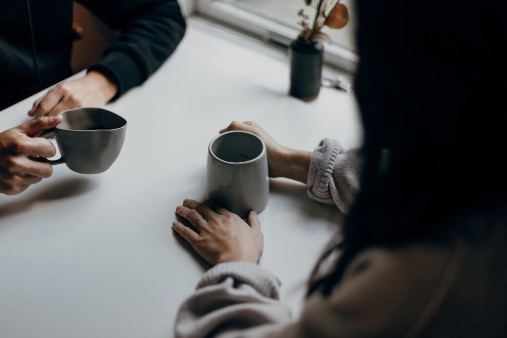 Two women talking while holding coffee mugs and one woman is disclosing to her colleague that she has MS Multiple Sclerosis